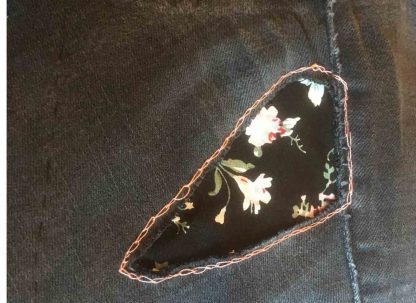 Black denim jeans with floral iron on reverse repair patches by vintage-patch.co.uk. The pretty floral fabric shows through the torn area and is decoratively stitched