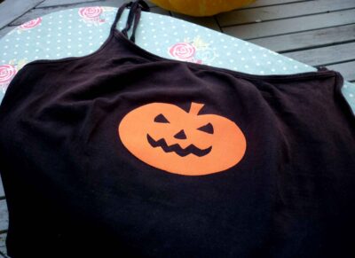 Black camsiole vest top with orange iron on pumpkin face motif cooling on ironing board after application