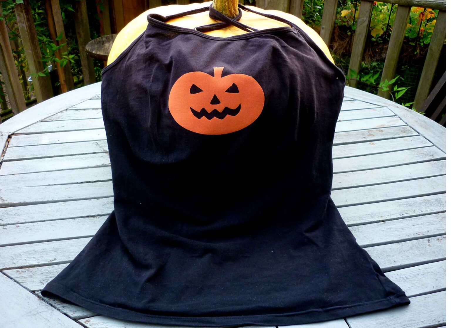 black strappy camisole vest top with orange pumpkin face motif on the front draped over a real pumpkin fruit