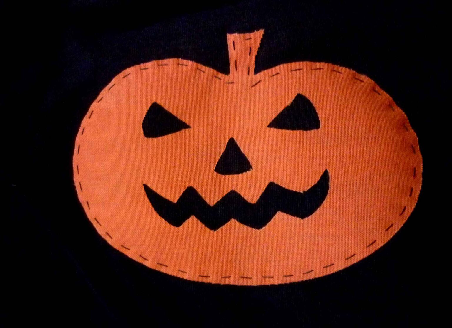 orange iron on pumpkin face motif applied to black top with running stitch decoration